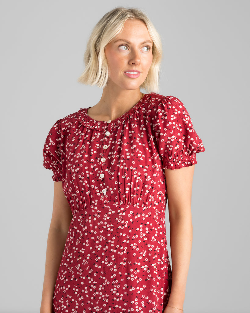 Model wearing a red with white floral print, short sleeve, round neck with ruffle details, maxi length slip dress.