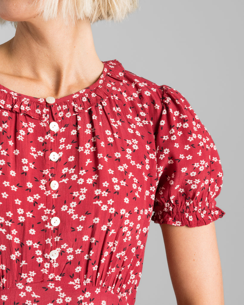 Model wearing a red with white floral print, short sleeve, round neck with ruffle details, maxi length slip dress.