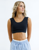 Woman wearing a black cropped tank top and light blue striped pants on a white background