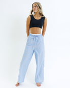 Woman wearing a black cropped tank top and light blue striped pants on a white background
