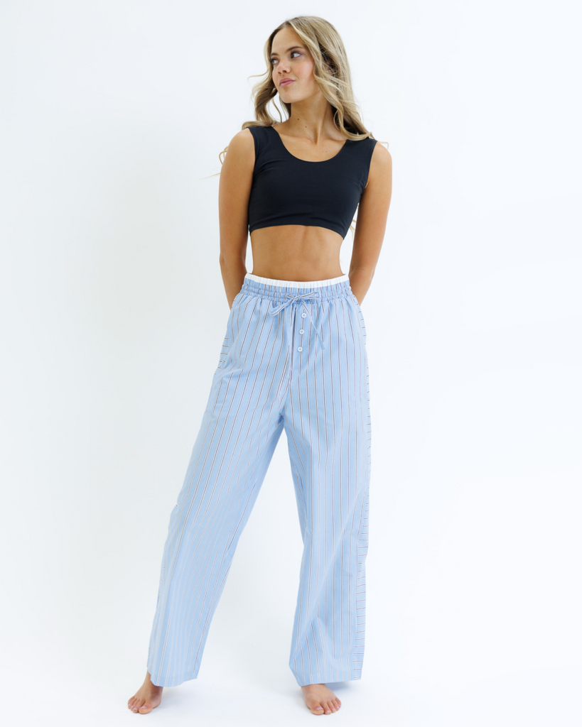 Woman wearing a black cropped tank top and light blue striped pants on a white background