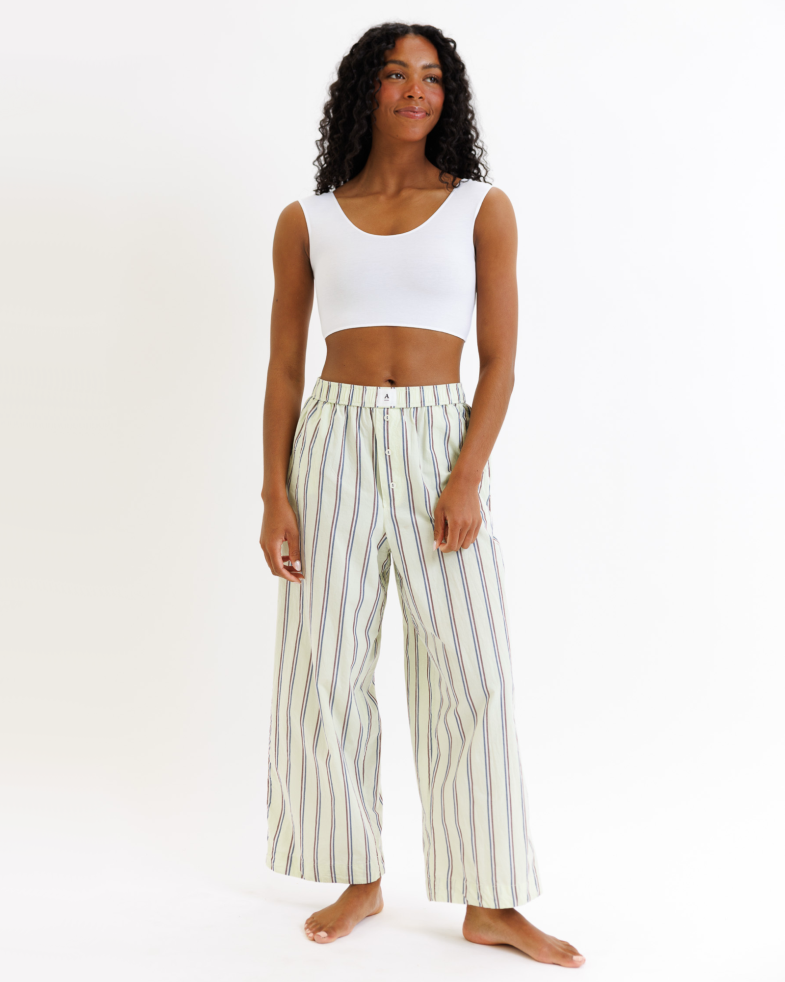 Woman wearing a white cropped tank top and striped pants on a white background