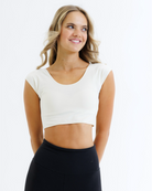 Woman wearing a cream colored cropped layering top and black pants on a white background