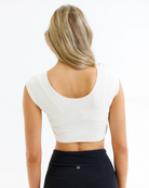 Woman wearing a cream colored cropped layering top and black pants on a white background
