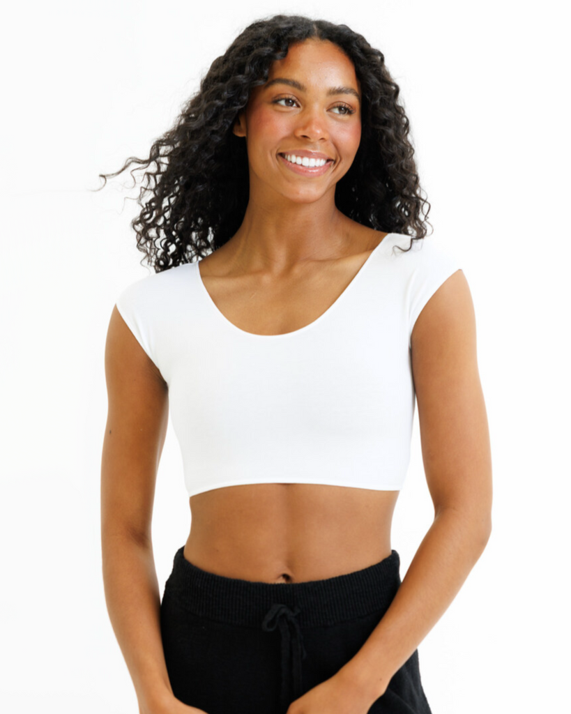 Woman wearing a white cropped layering top and black pants on a white background