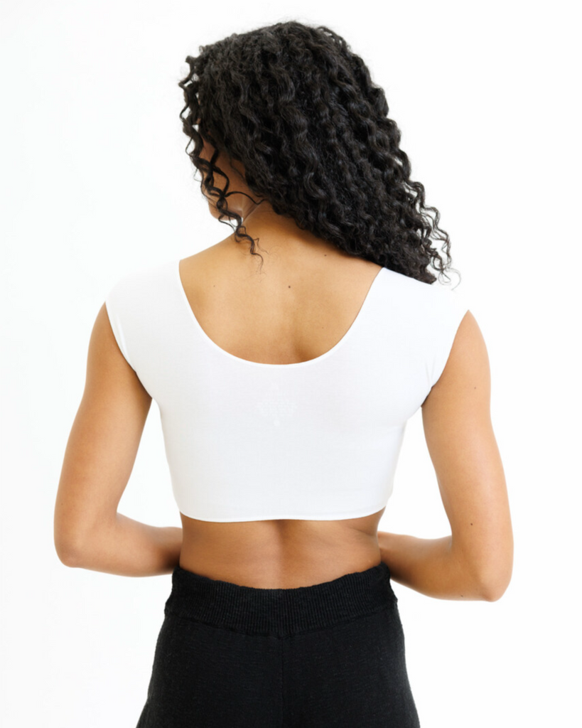 Woman wearing a white cropped layering top and black pants on a white background