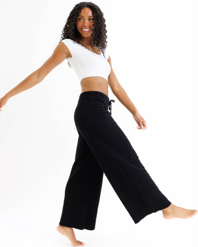 Woman wearing a white cropped layering top and black wide-leg pants on a white background