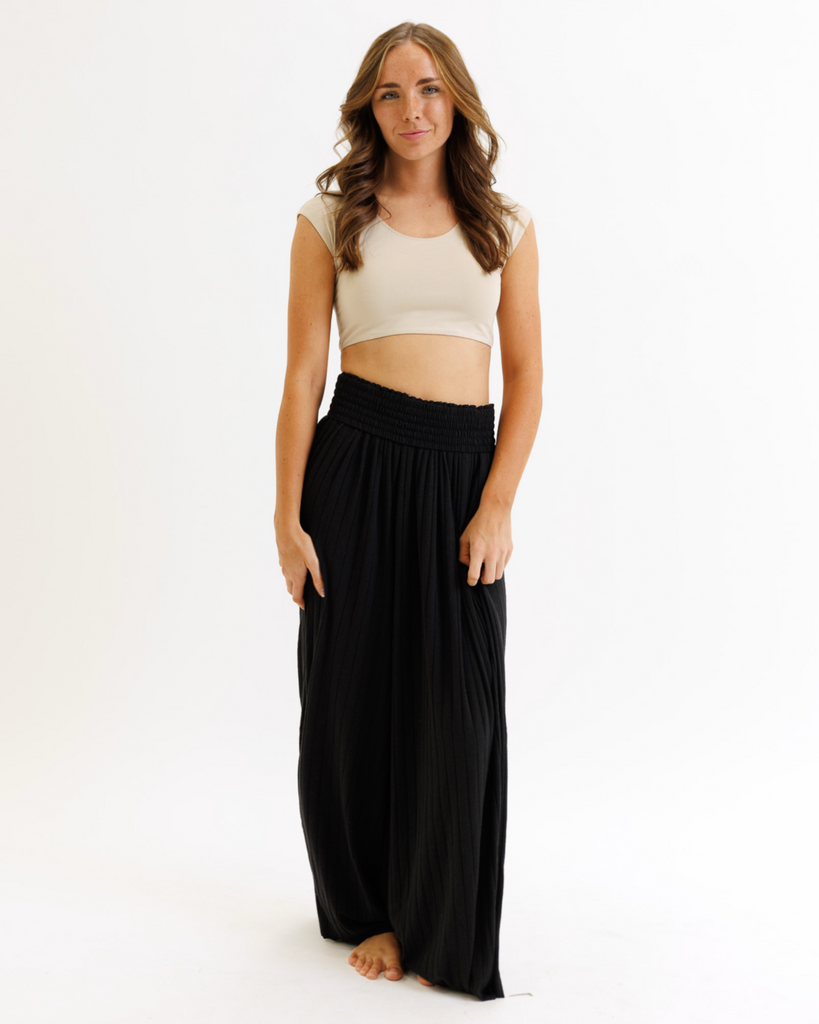 Woman wearing a beige cropped layering top and black flowing pants on a white background