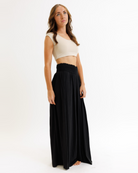 Woman wearing a beige cropped layering top and black flowing pants on a white background