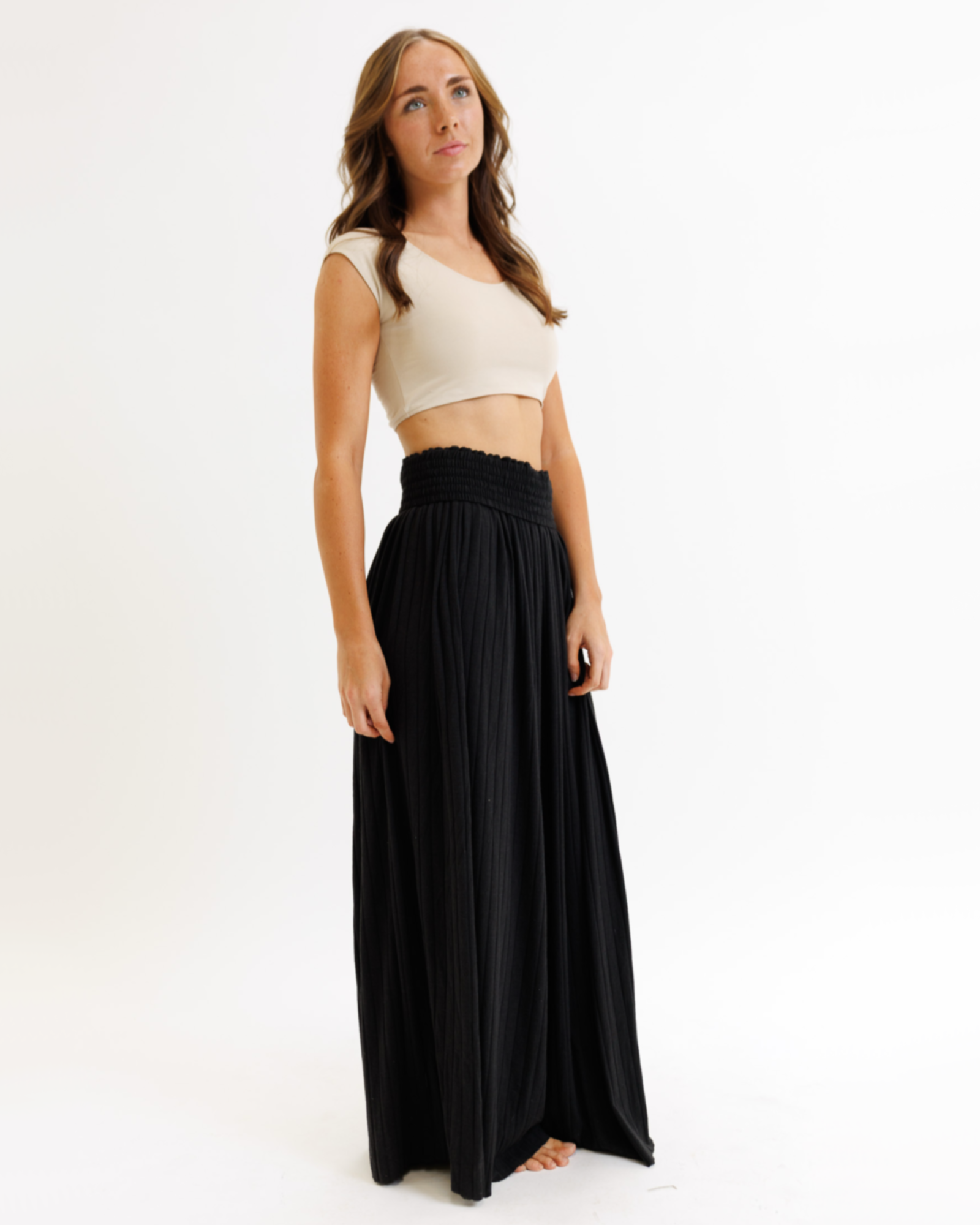 Woman wearing a beige cropped layering top and black flowing pants on a white background