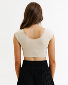 Woman wearing a beige cropped layering top and black flowing pants on a white background