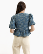 Woman wearing a blue denim floral blouse with puffed sleeves on a white background
