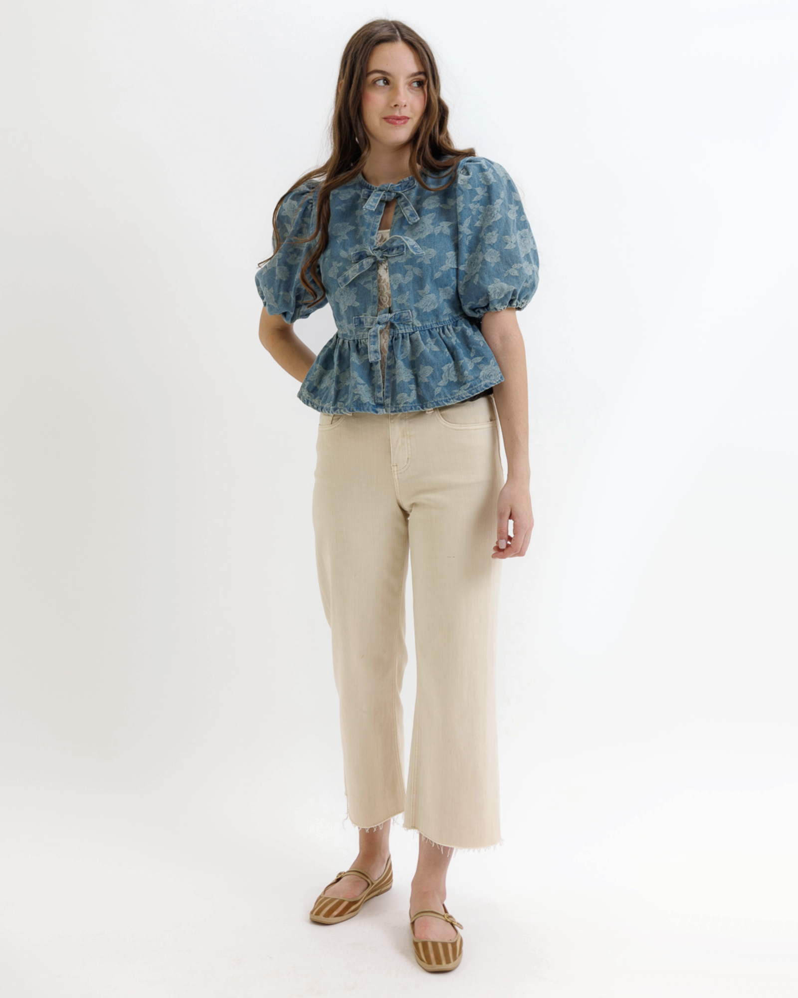 Woman wearing a blue denim floral blouse with puffed sleeves on a white background