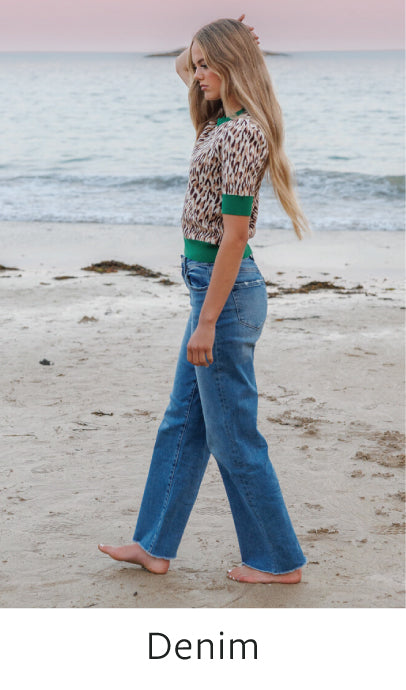 Woman walking on a beach wearing a leopard print top and blue jeans.