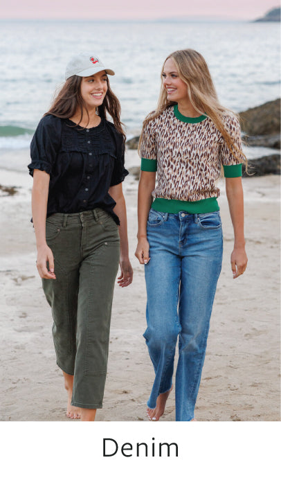 Two women walking on a beach, wearing denim jeans.