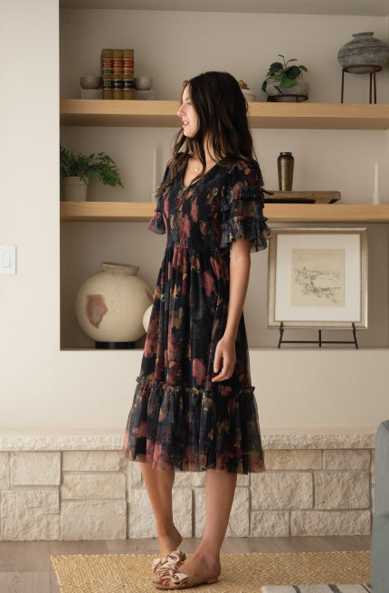 Model wearing a black with pink watercolor print, short sleeve, v-neck, midi length dress.