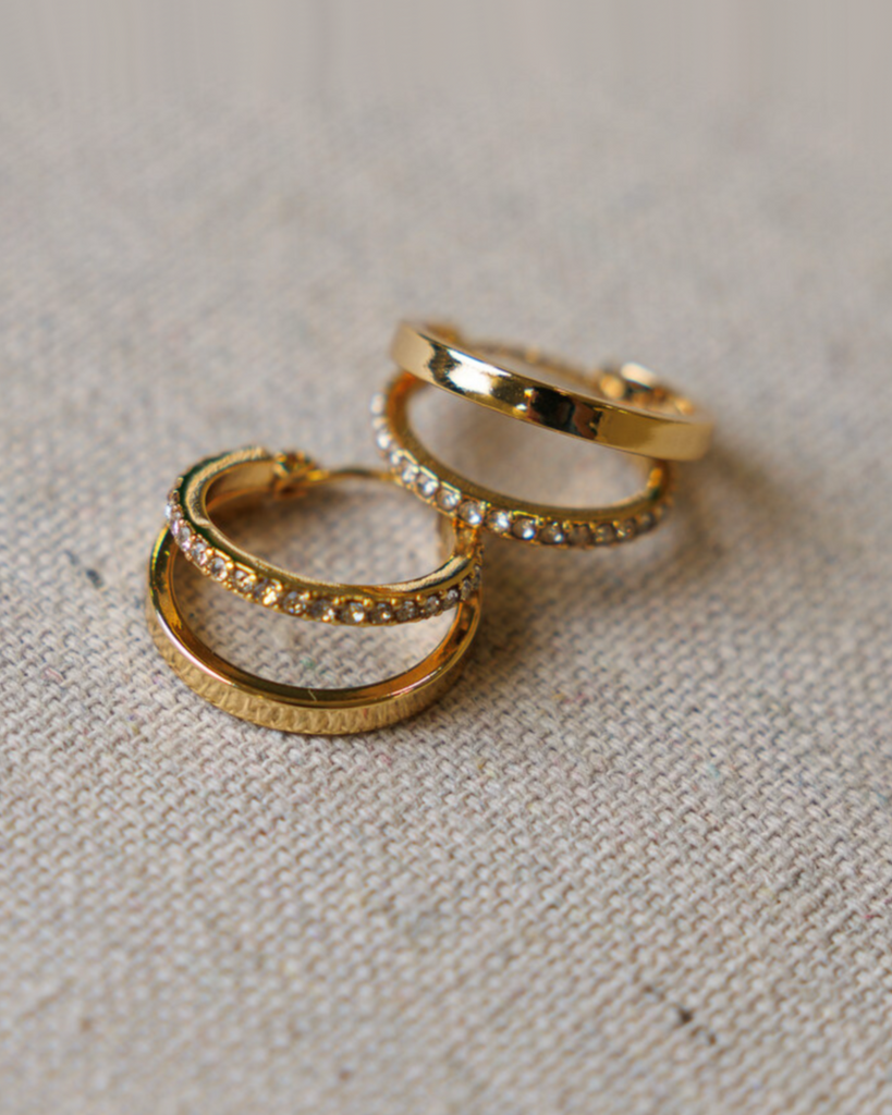 Gold hoop earrings with diamond details on a textured beige surface