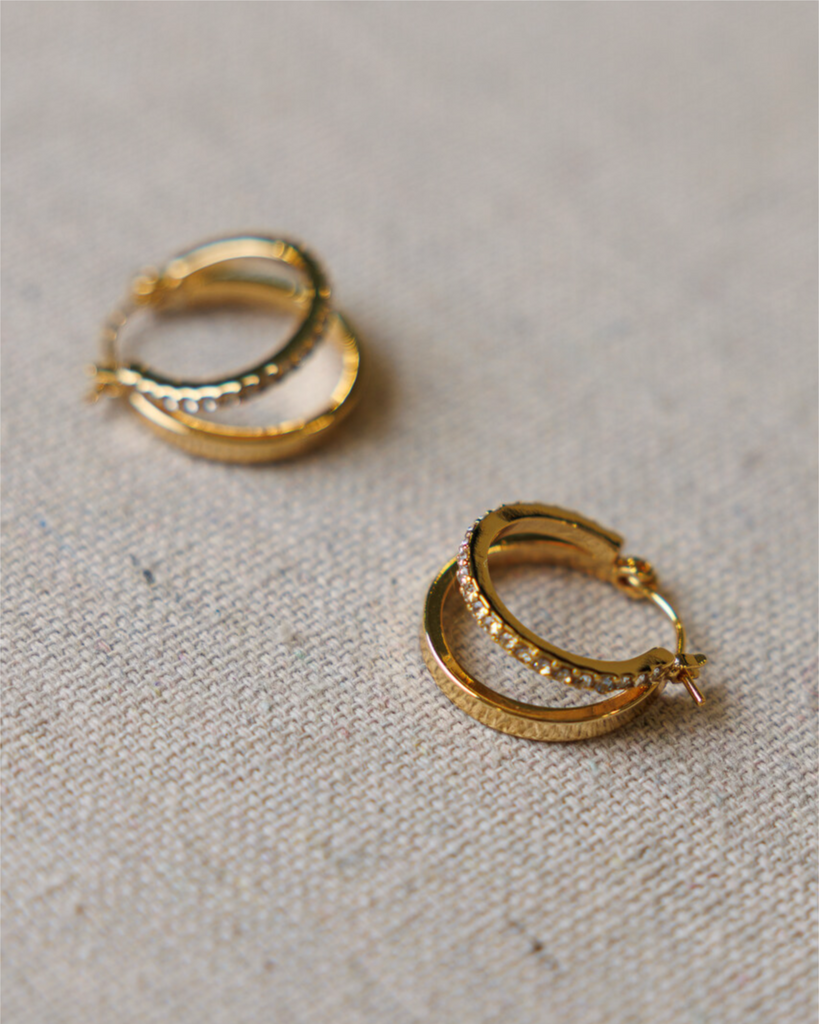 Gold hoop earrings with diamond details on a textured beige surface