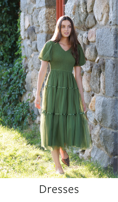 Woman wearing a green dress standing against a stone wall.