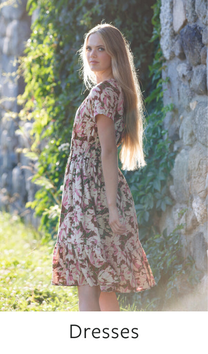 Woman wearing a floral dress standing against a stone wall with greenery
