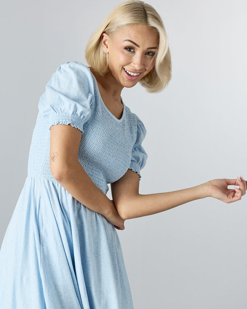 Woman in a blue short sleeved, knee length dress with smocking on bodice.