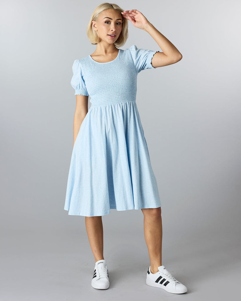 Woman in a blue short sleeved, knee length dress with smocking on bodice.