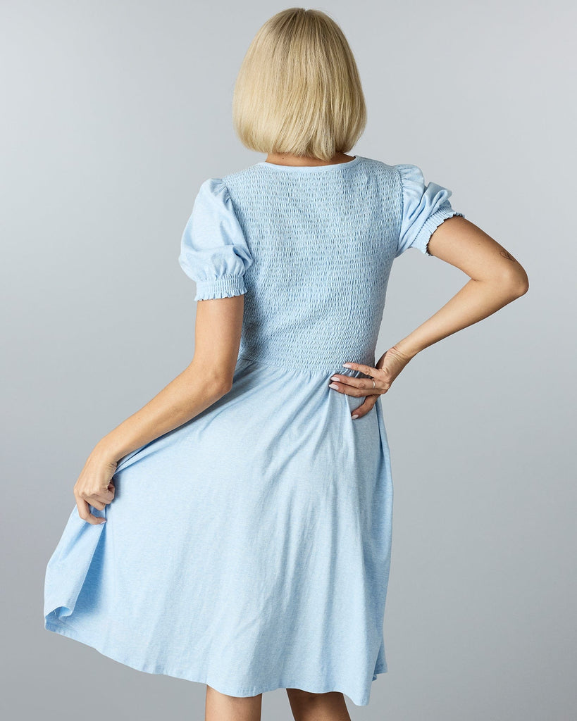 Woman in a blue short sleeved, knee length dress with smocking on bodice.