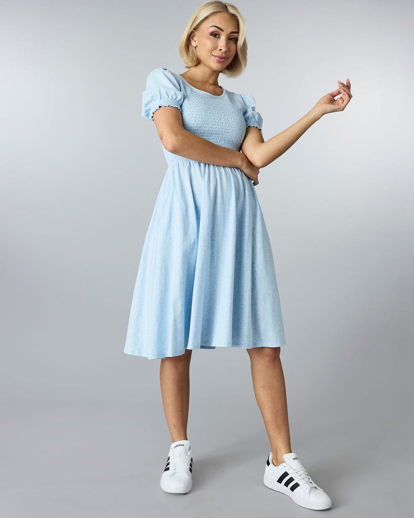 Woman in a blue short sleeved, knee length dress with smocking on bodice.