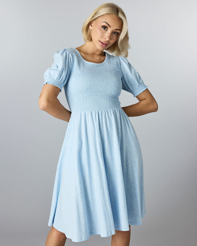 Woman in a blue short sleeved, knee length dress with smocking on bodice.