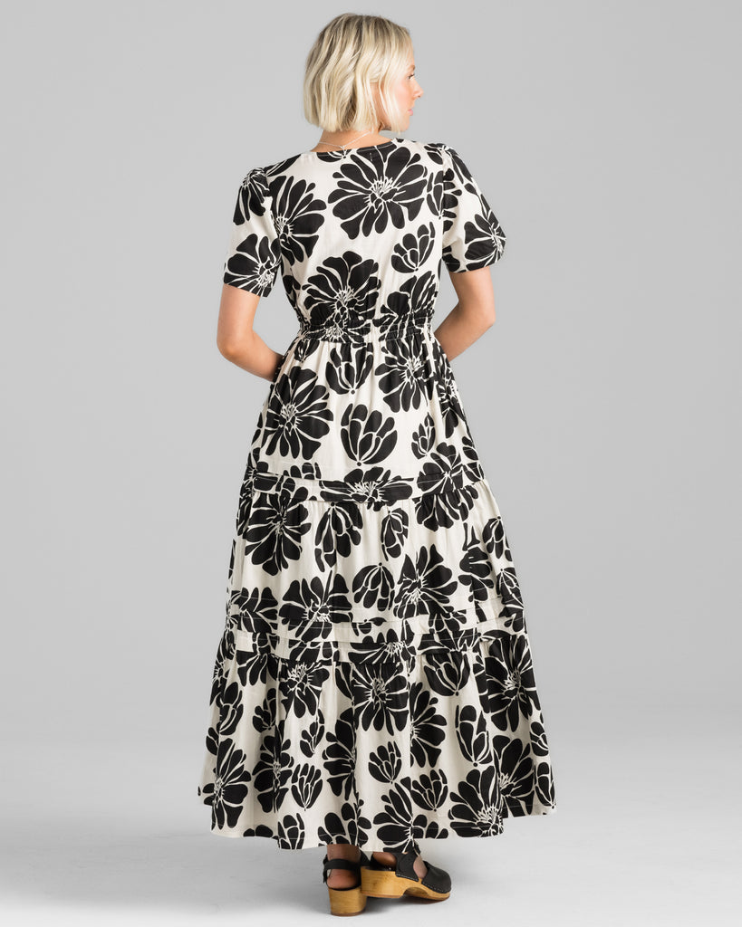 Model wearing a white with black floral print short sleeve, v-neck maxi dress with elastic waistband.