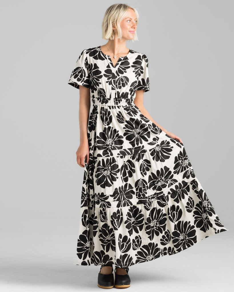 Model wearing a white with black floral print short sleeve, v-neck maxi dress with elastic waistband.