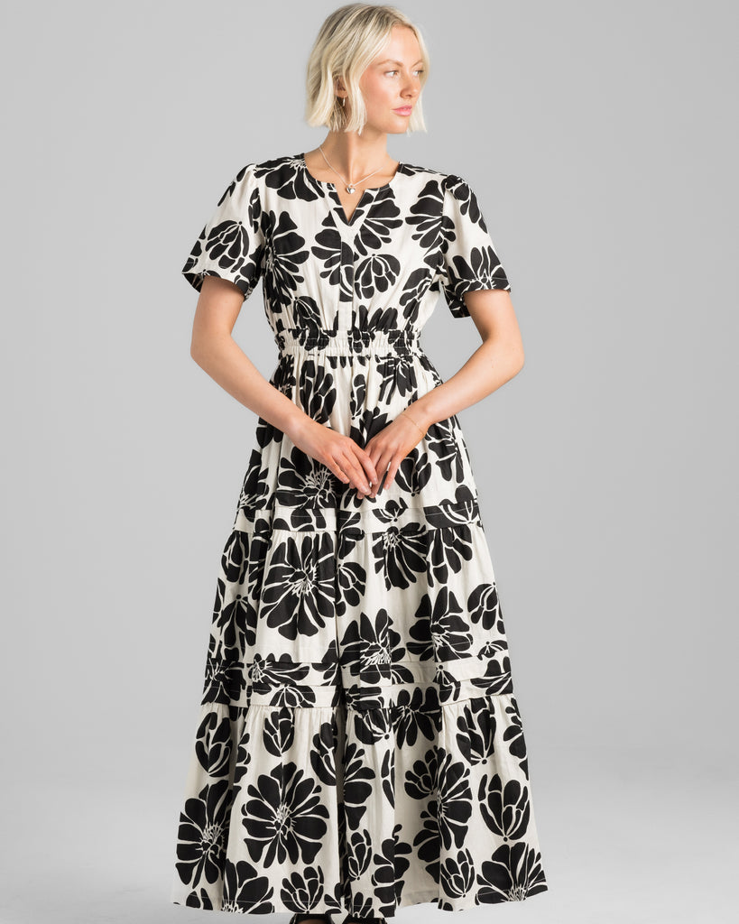 Model wearing a white with black floral print short sleeve, v-neck maxi dress with elastic waistband.