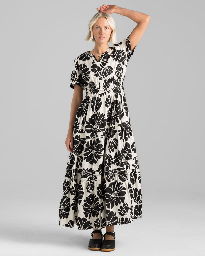 Model wearing a white with black floral print short sleeve, v-neck maxi dress with elastic waistband.