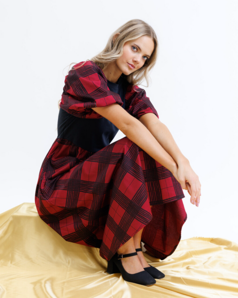 Woman wearing a red and black plaid dress sitting on a gold surface with a white background