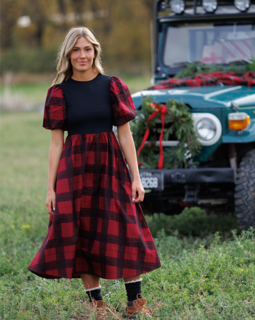 Woman wearing a red and black plaid dress standing in front of a green car in the outdoors