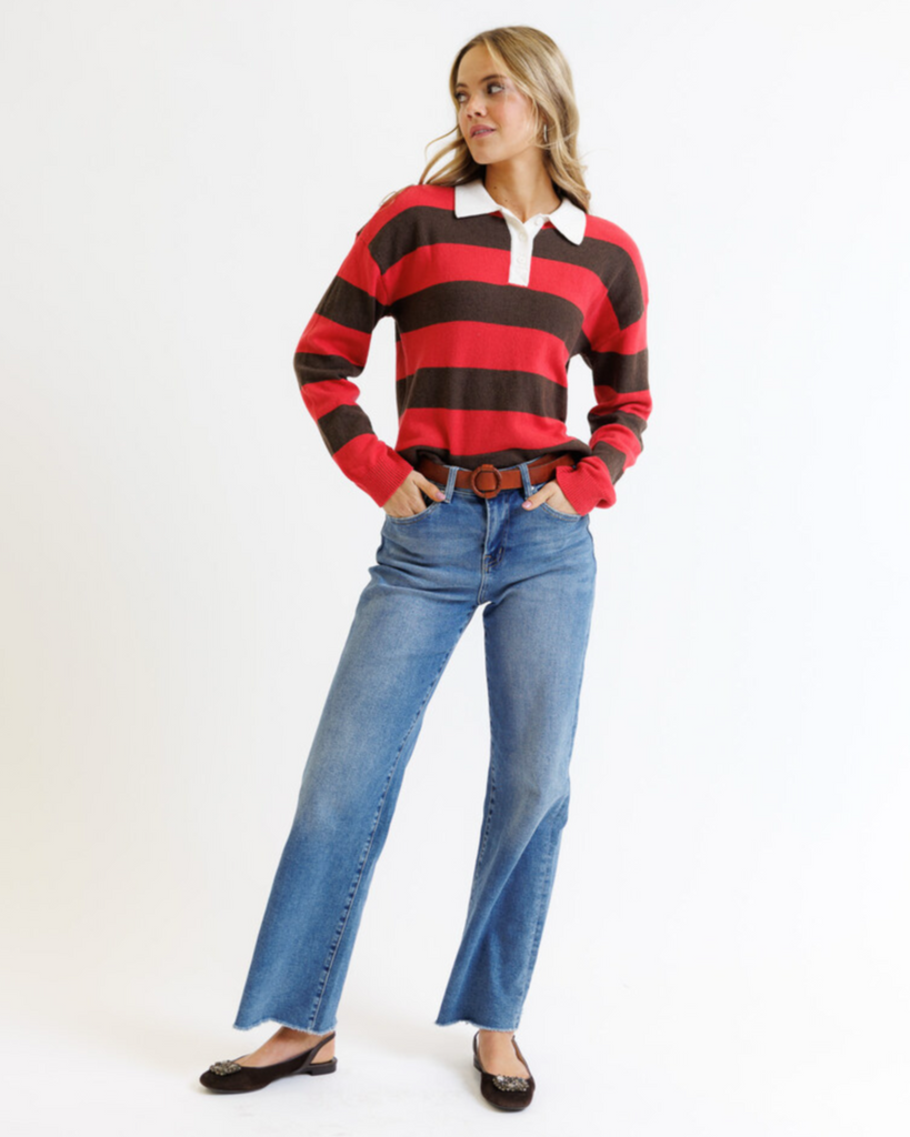 Woman wearing a red and brown striped sweater with blue jeans on a white background