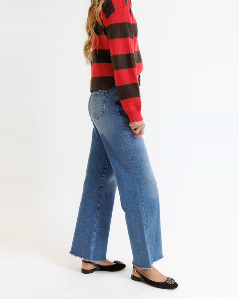 Woman wearing a red and brown striped sweater with blue jeans on a white background