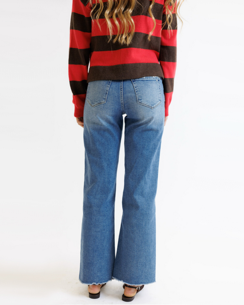 Woman wearing a red and brown striped sweater with blue jeans on a white background