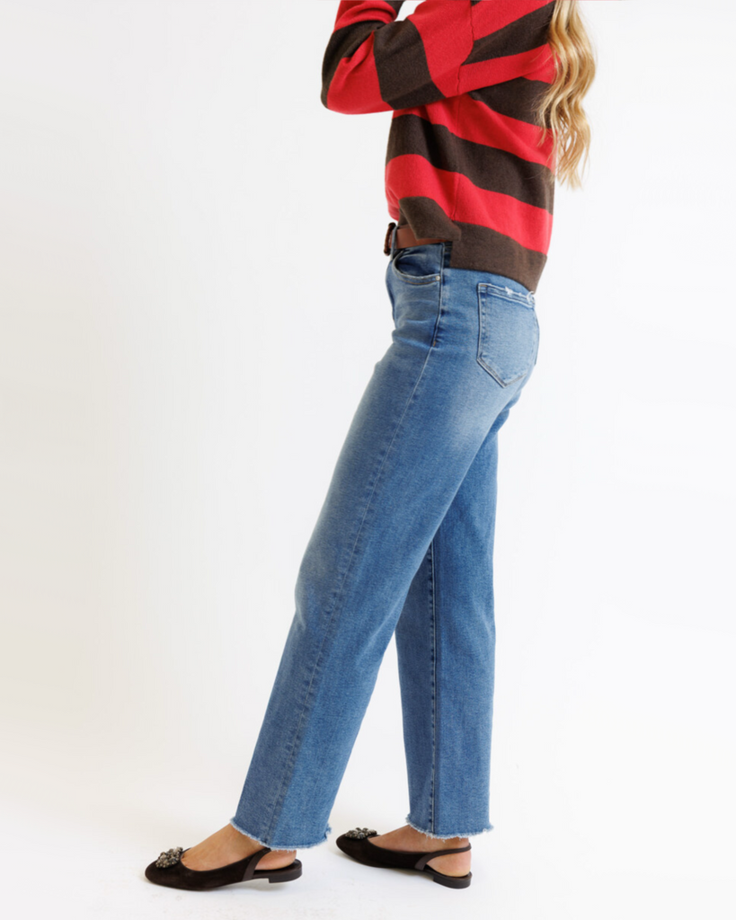Woman wearing a red and brown striped sweater with blue jeans on a white background