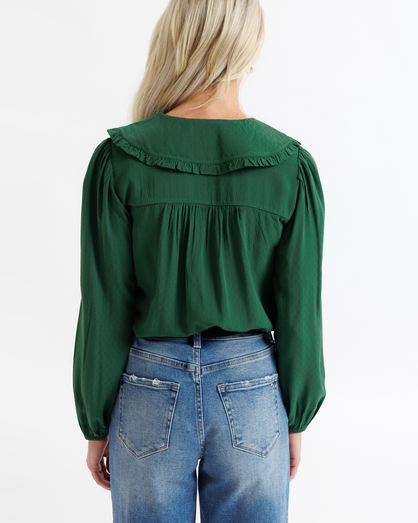 Green blouse with ruffled details and blue jeans on a white background