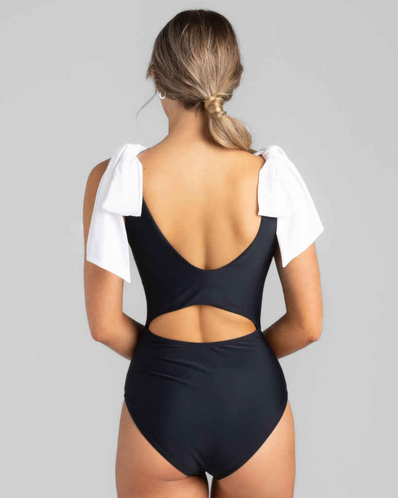 Model wearing a black one-piece swimsuit with white ties on shoulders.