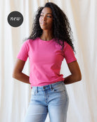 A woman wearing a pink short-sleeve crewneck t-shirt and light blue jeans, standing against a fabric backdrop.