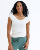 Woman wearing a cream colored layering top and green knit pants on a white background