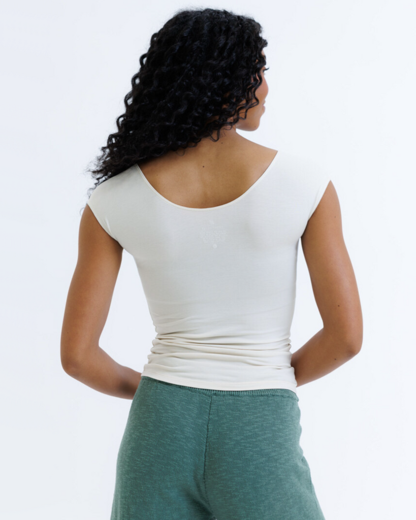 Woman wearing a cream colored layering top and green knit pants on a white background
