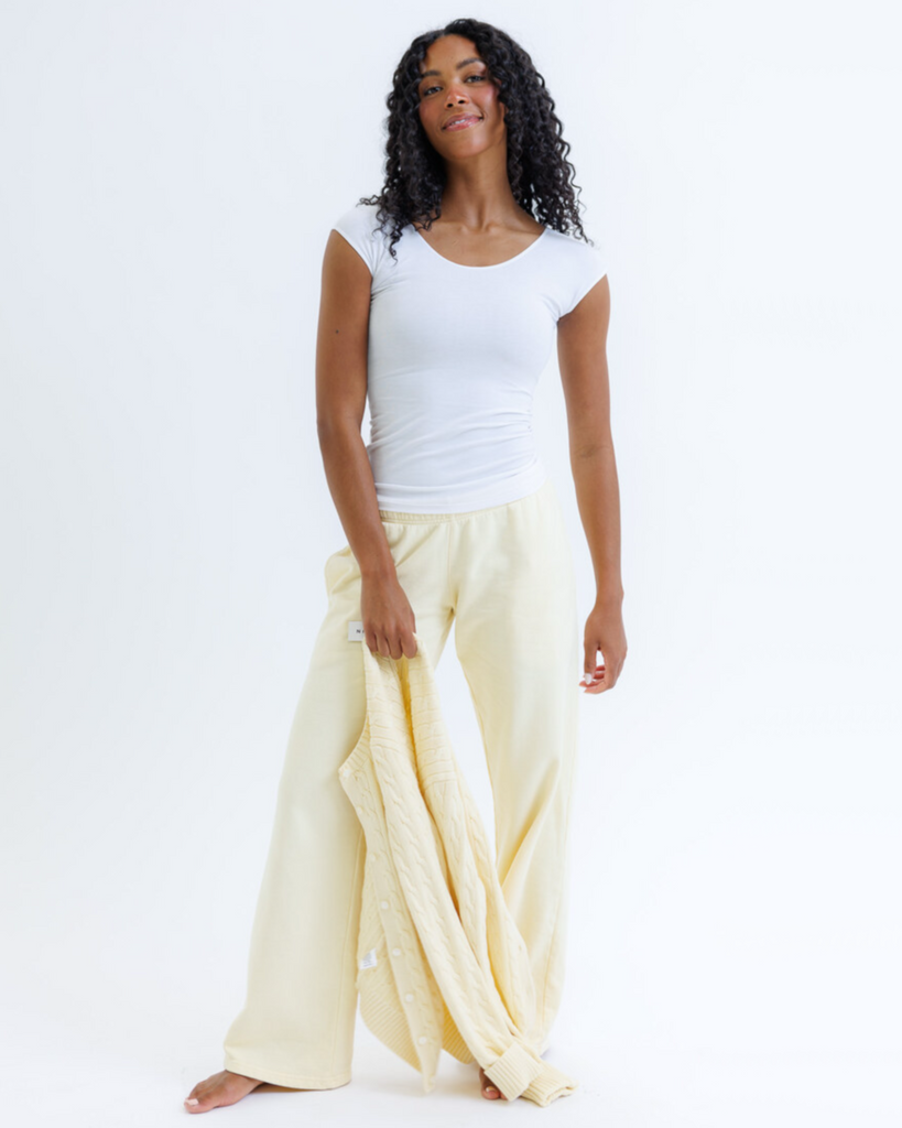 Woman wearing a white layering top with yellow sweatpants on a white background