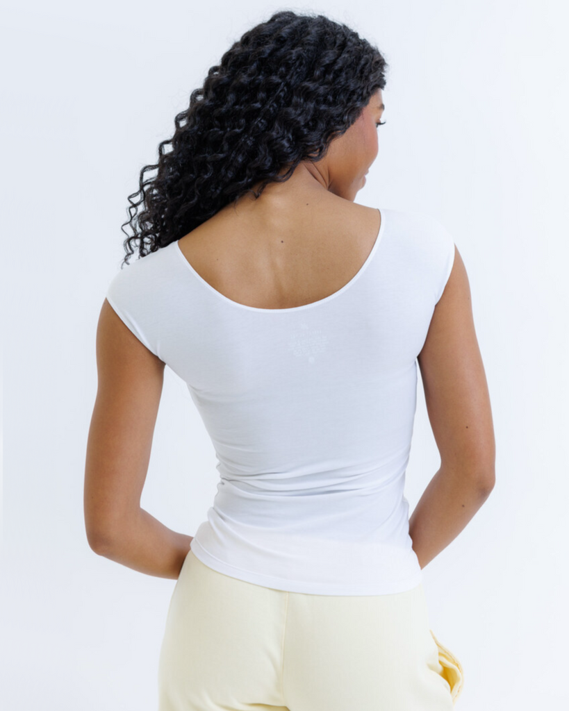 Woman wearing a white layering top with yellow sweatpants on a white background