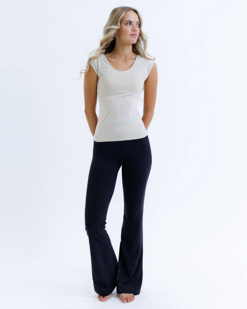Woman wearing a nude cap sleeve layering top and black pants on a white background