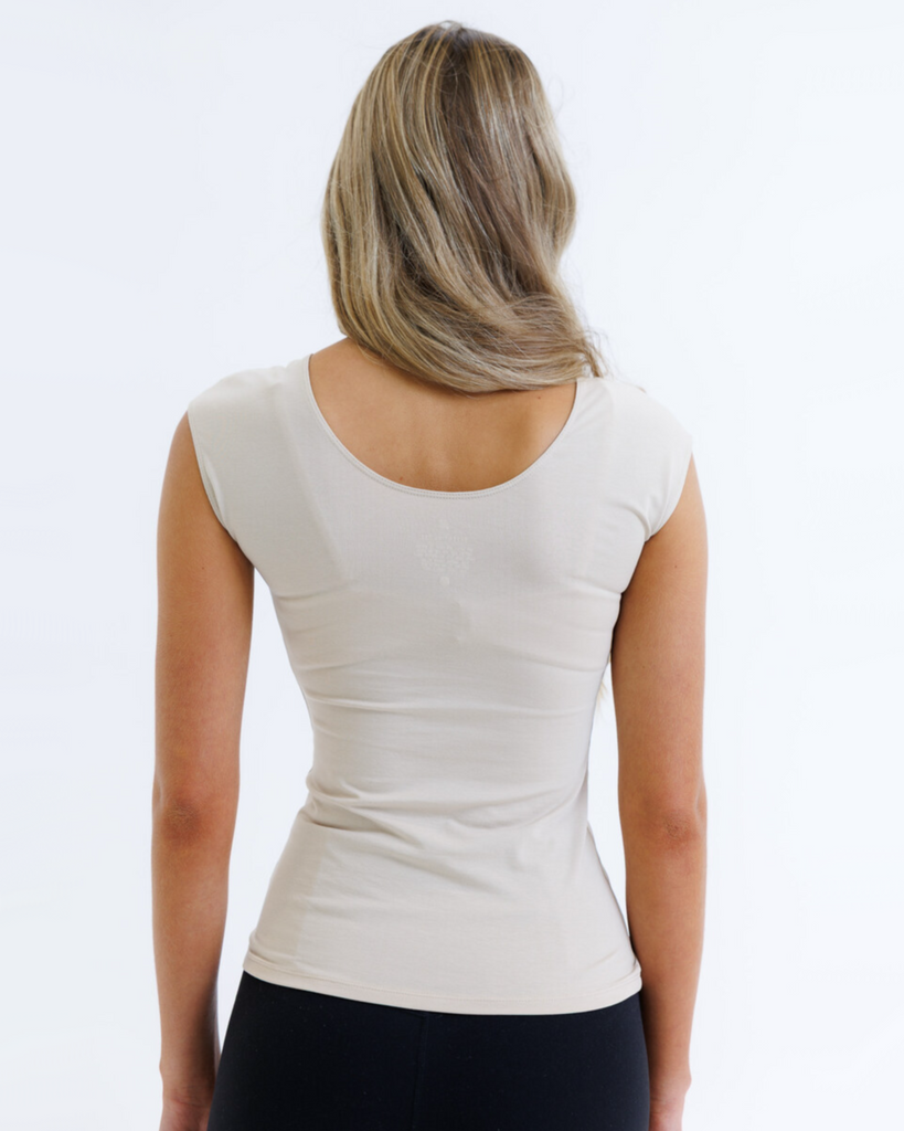 Woman wearing a nude cap sleeve layering top on a white background