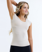 Woman wearing a nude cap sleeve layering top on a white background