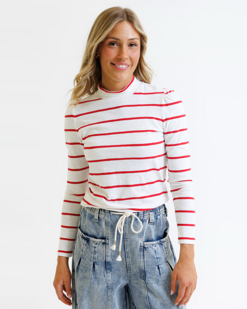 Woman wearing a white long-sleeve shirt with red stripes and blue jeans on a white background